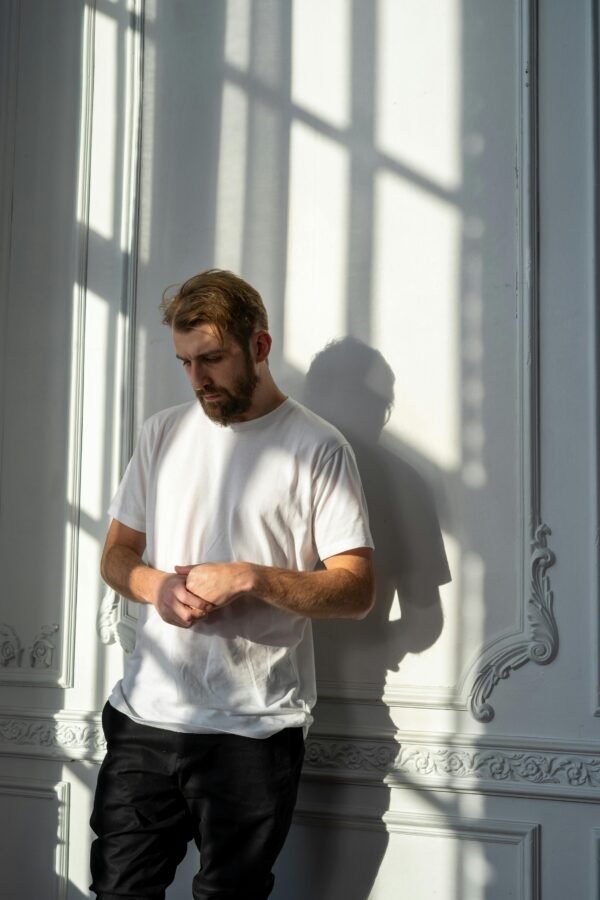 pexels-photo-4101142-4101142 A thoughtful bearded man in a white t-shirt stands in a sunlit room with ornate walls.